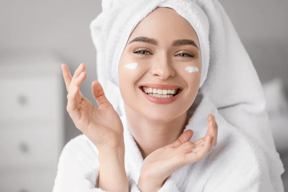 Mujer con toalla en el pelo y crema en la cara, sonriendo